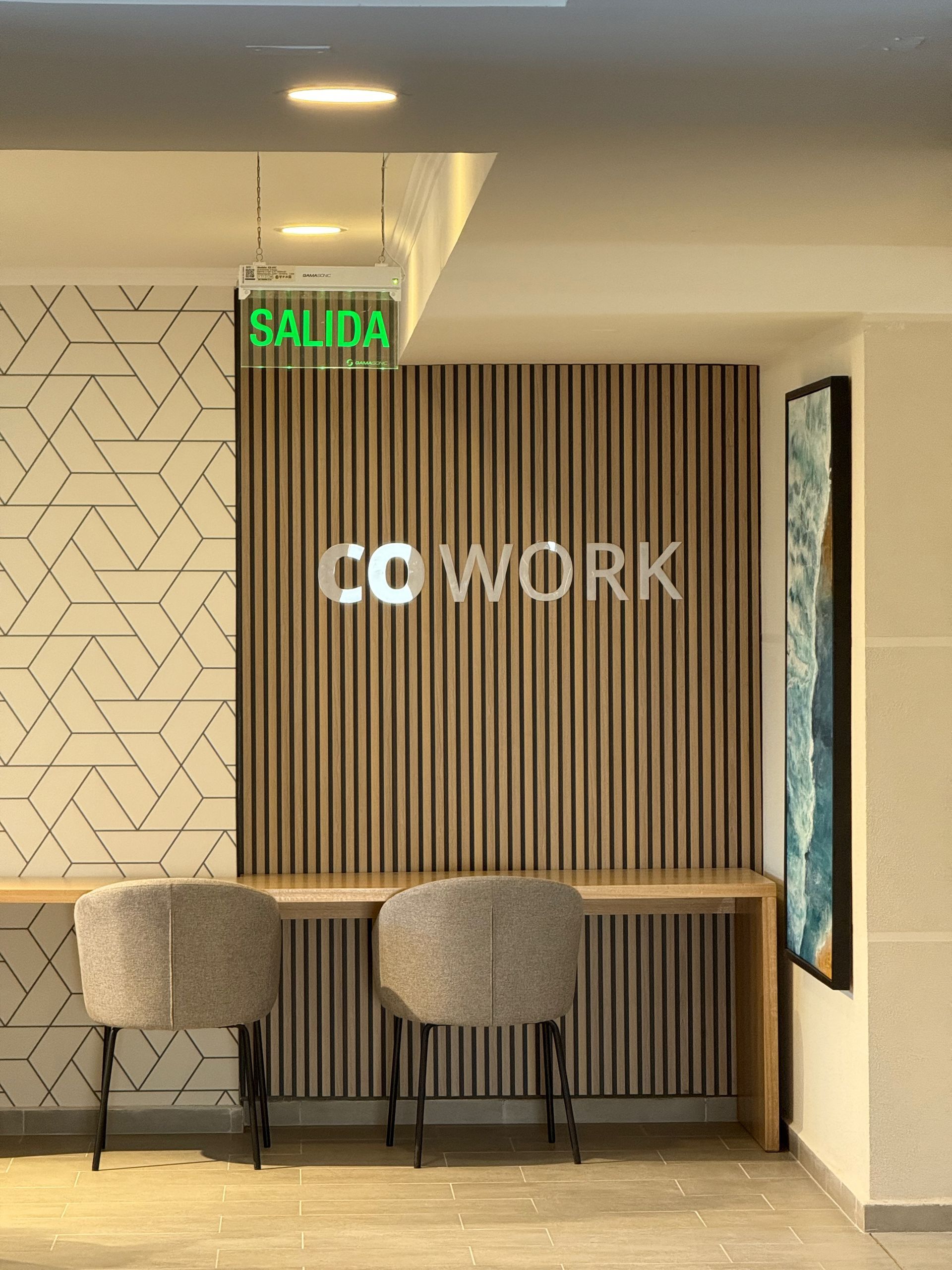 Espacio de coworking moderno con taburetes de bar, pared de listones de madera y letrero de salida verde.