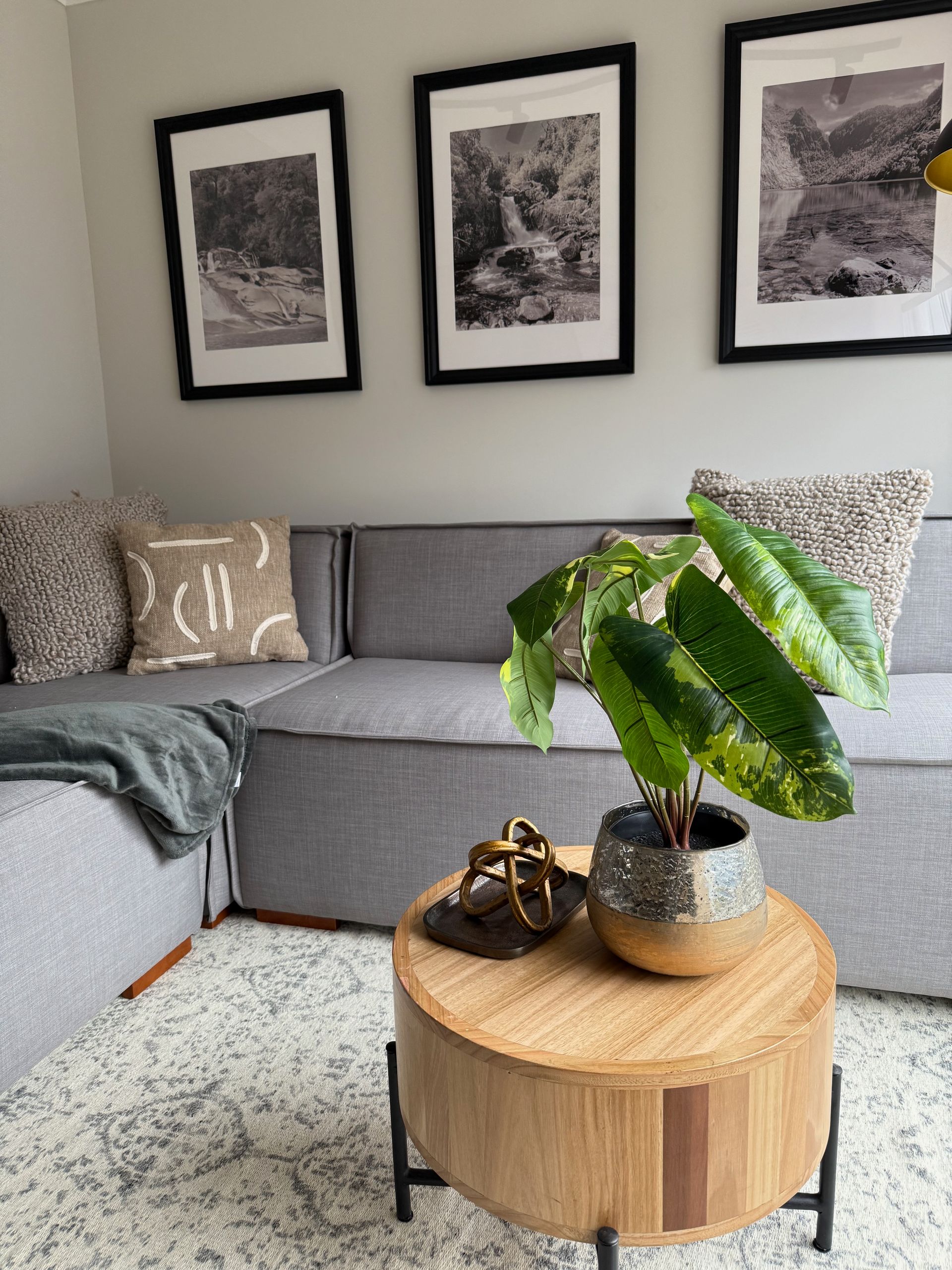 Sala de estar moderna con sofá modular gris, cuadros enmarcados en la pared y una mesa de centro de madera.