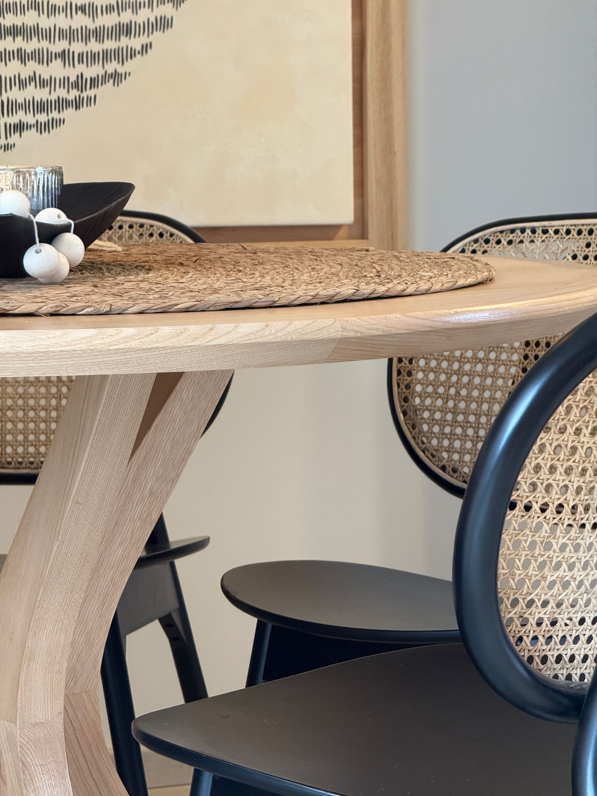 Mesa de comedor con sillas de mimbre y decoración neutra en una habitación luminosa.
