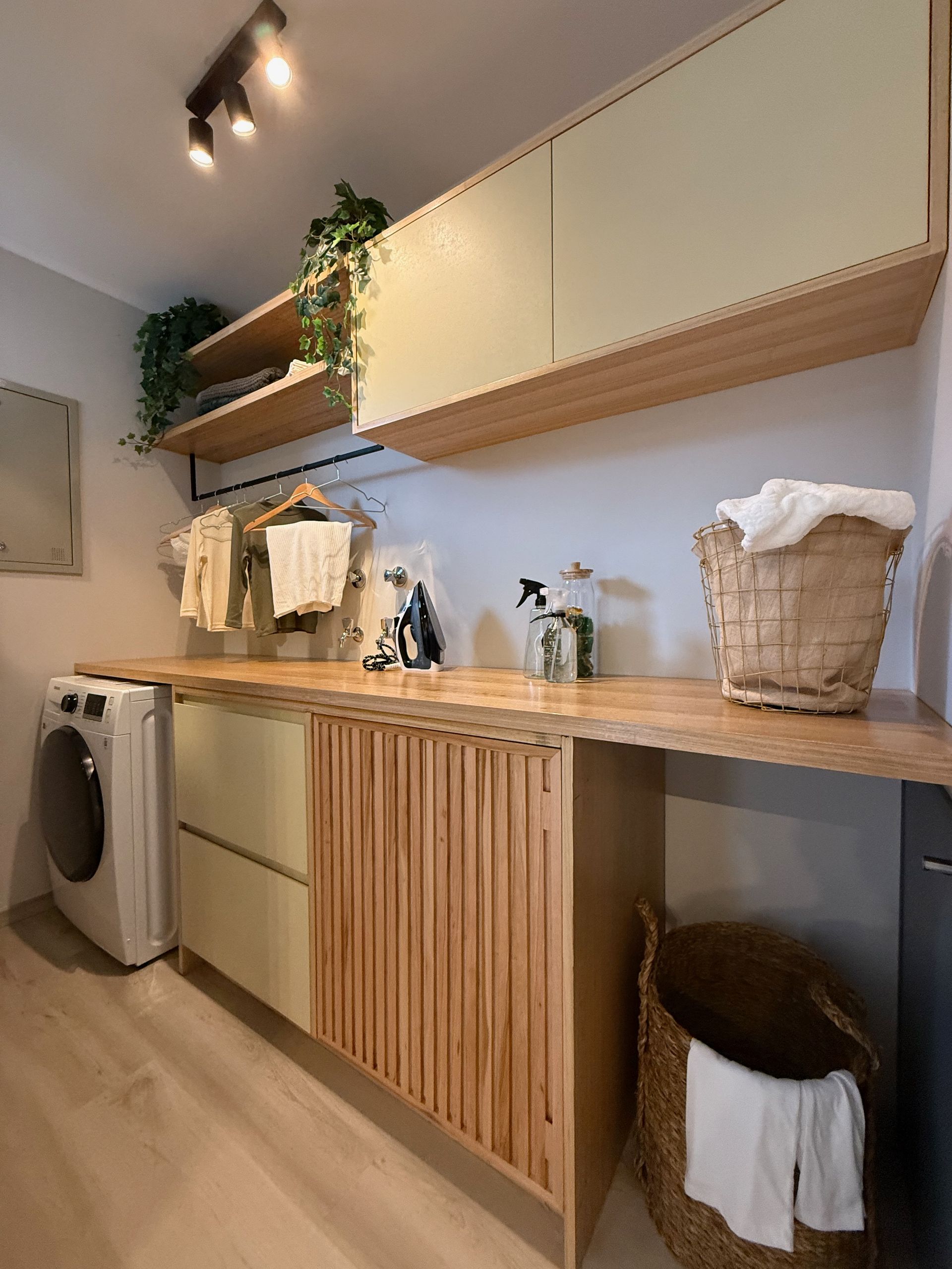 Lavadero moderno con encimera de madera, armarios blancos, lavadora, estantes de almacenamiento y cestas de mimbre.
