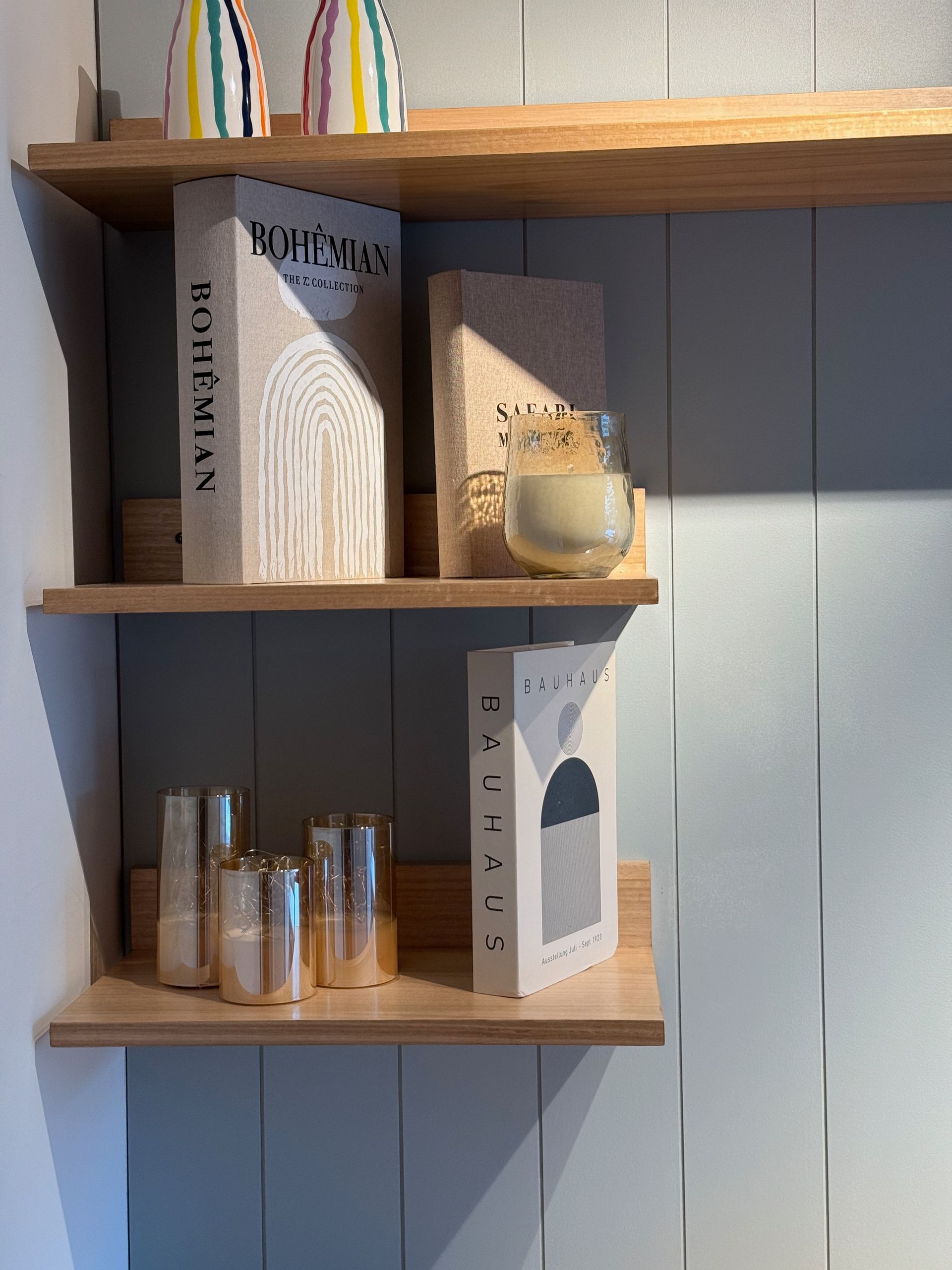 Estanterías de madera con libros, botellas de vidrio y un pequeño jarrón decorativo.