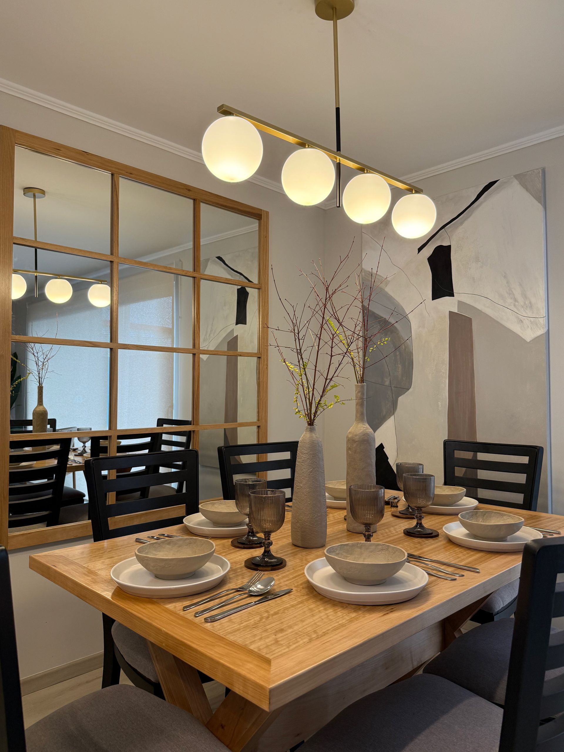 Comedor moderno con mesa de madera, vajilla puesta y lámparas colgantes esféricas.