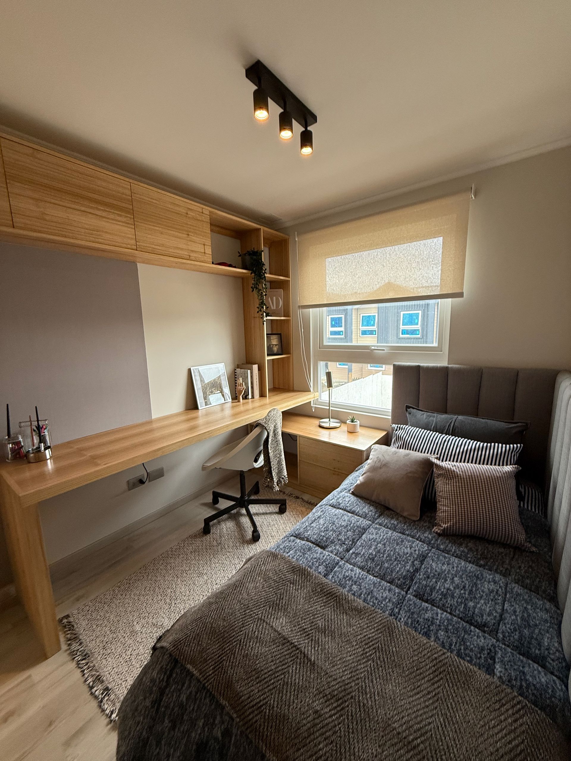 Acogedor despacho y dormitorio con escritorio de madera, silla, cama individual y ventana con persianas y vistas a la ciudad.