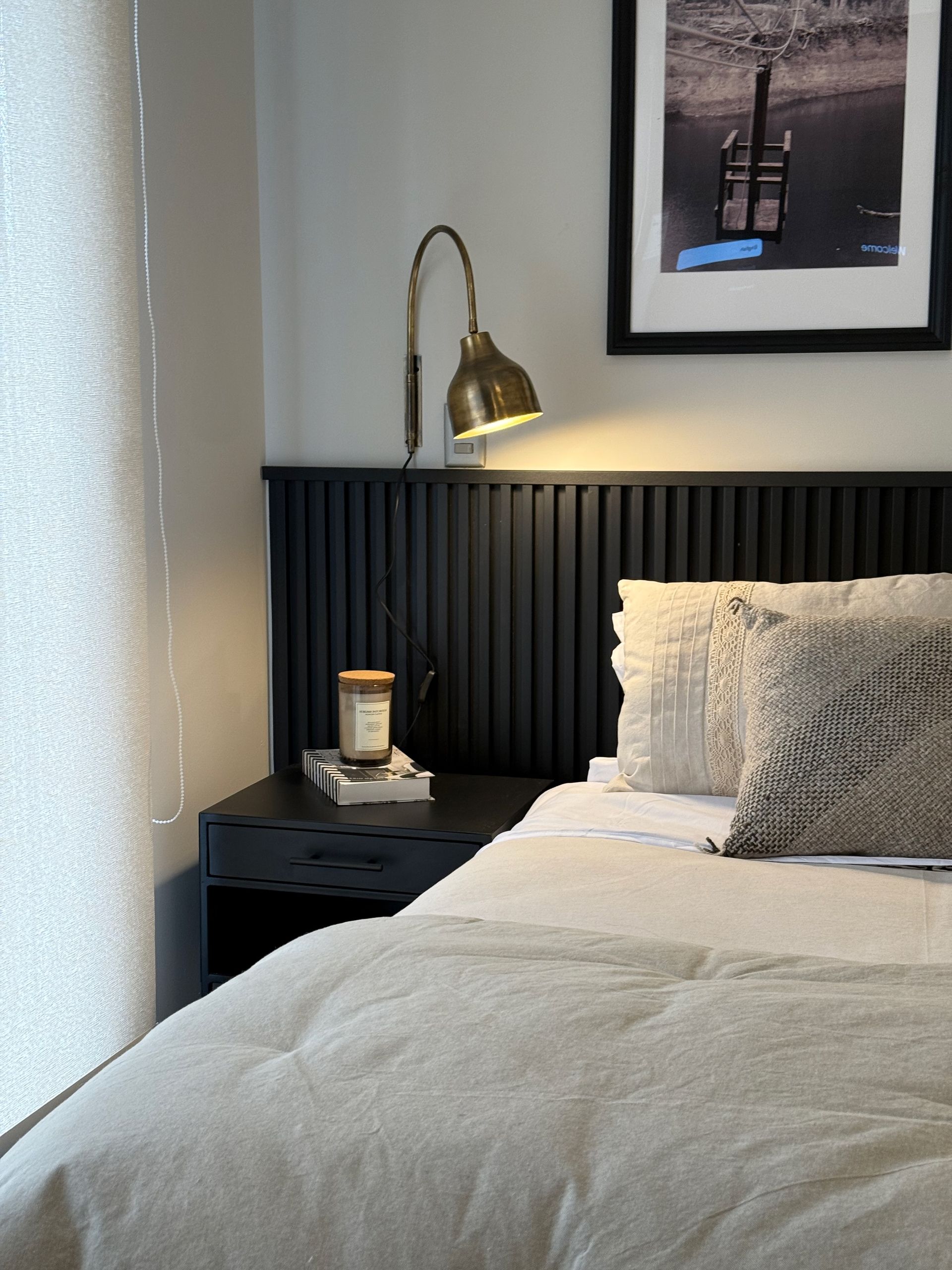 Habitación acogedora con cama, cabecero negro, lámpara de noche y cuadro enmarcado.