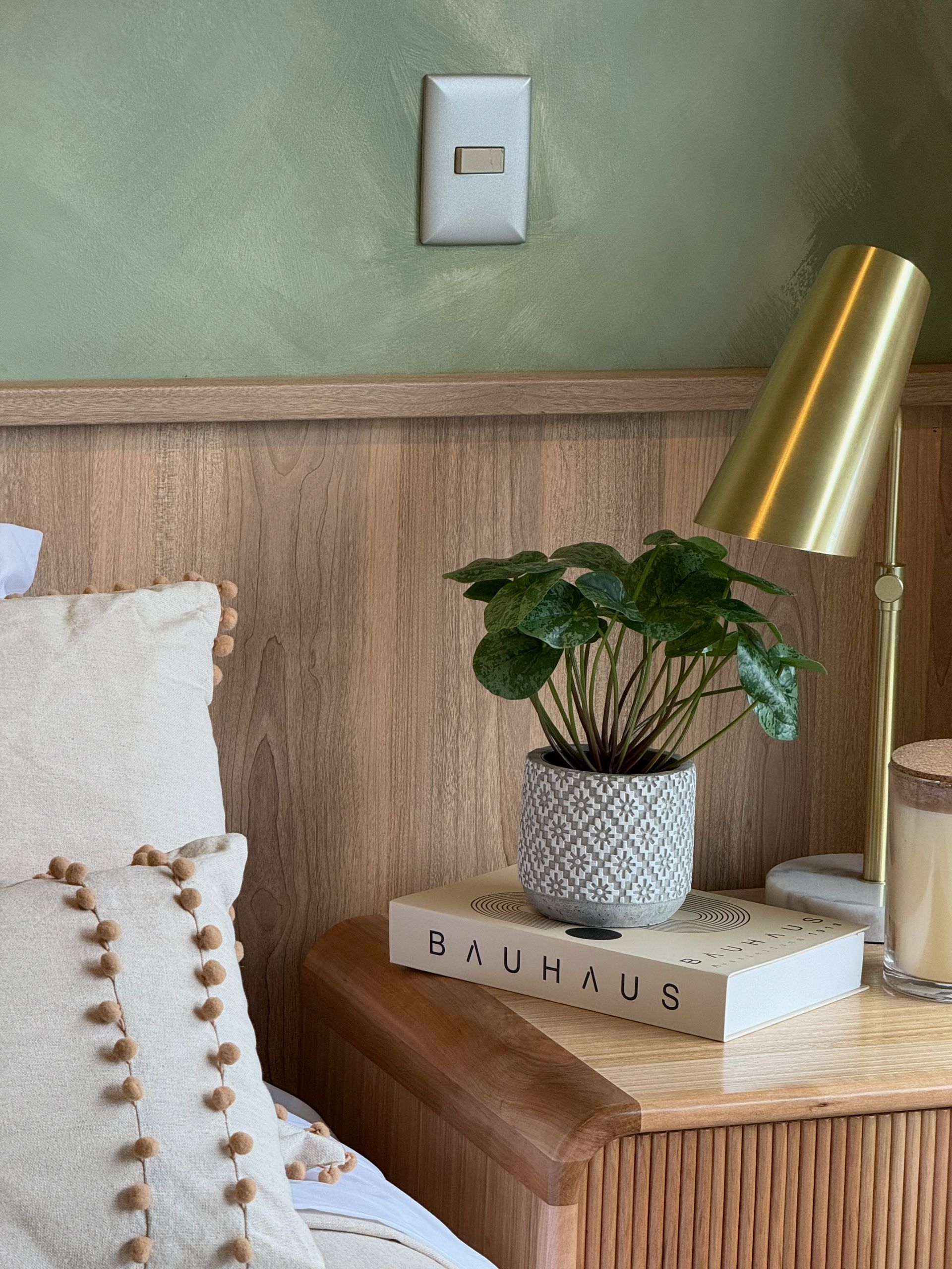 Acogedor rincón de dormitorio con una mesita de noche de madera, una planta, una lámpara y libros.
