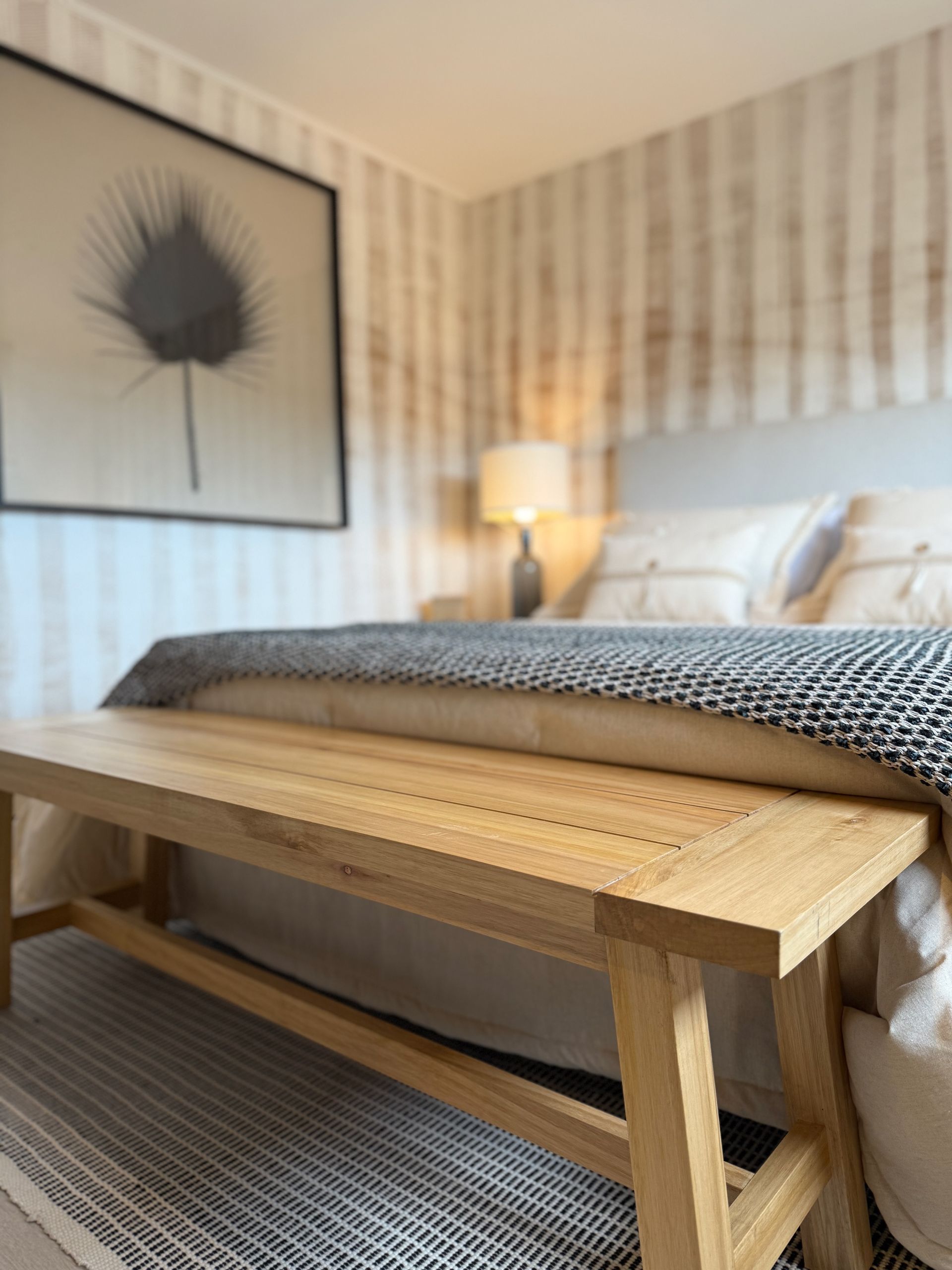 Acogedora habitación con banco de madera, papel pintado a rayas, cuadros enmarcados y cama con ropa de cama estampada.