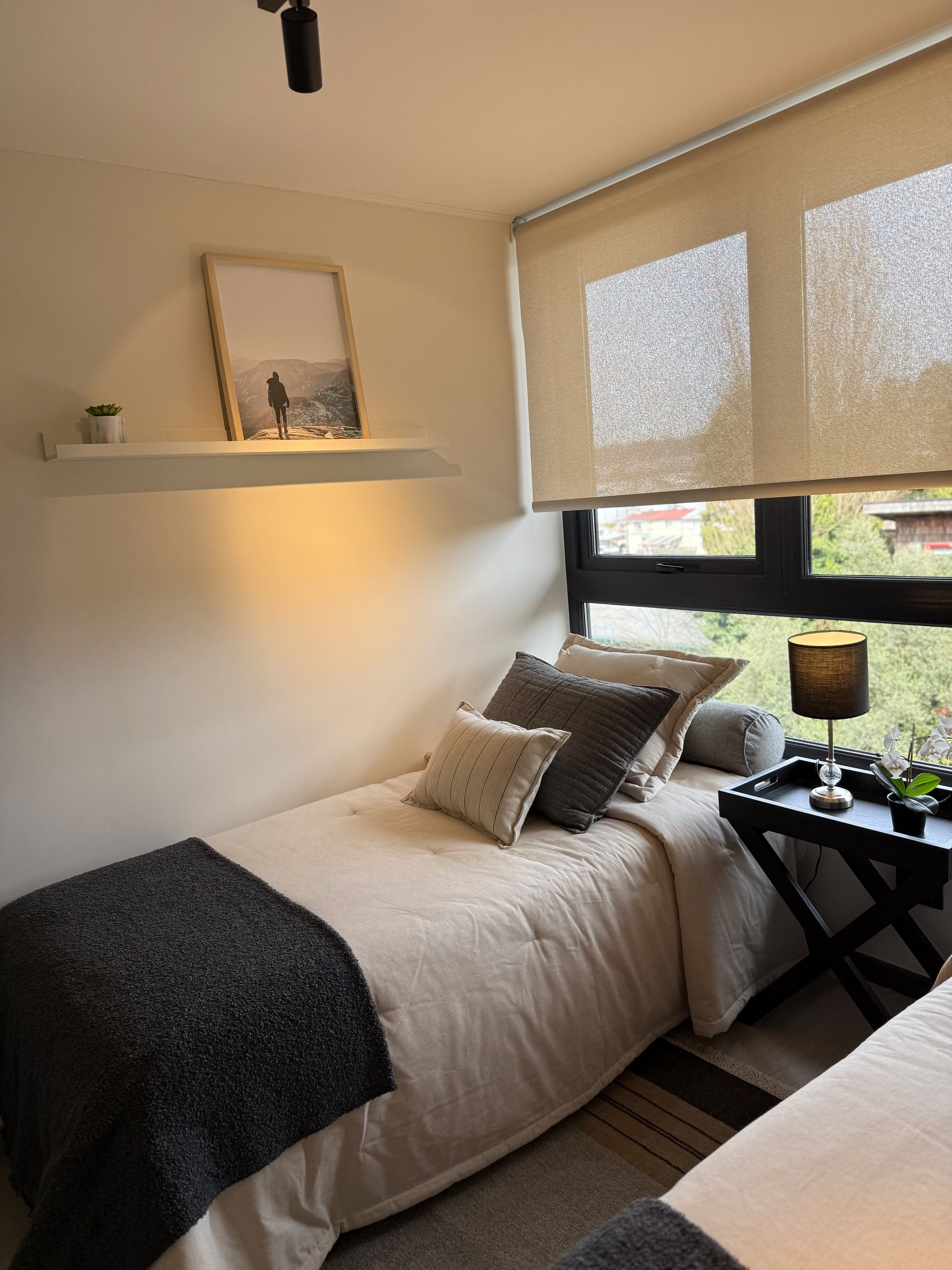 Habitación pequeña con dos camas individuales, ropa de cama blanca, manta oscura.