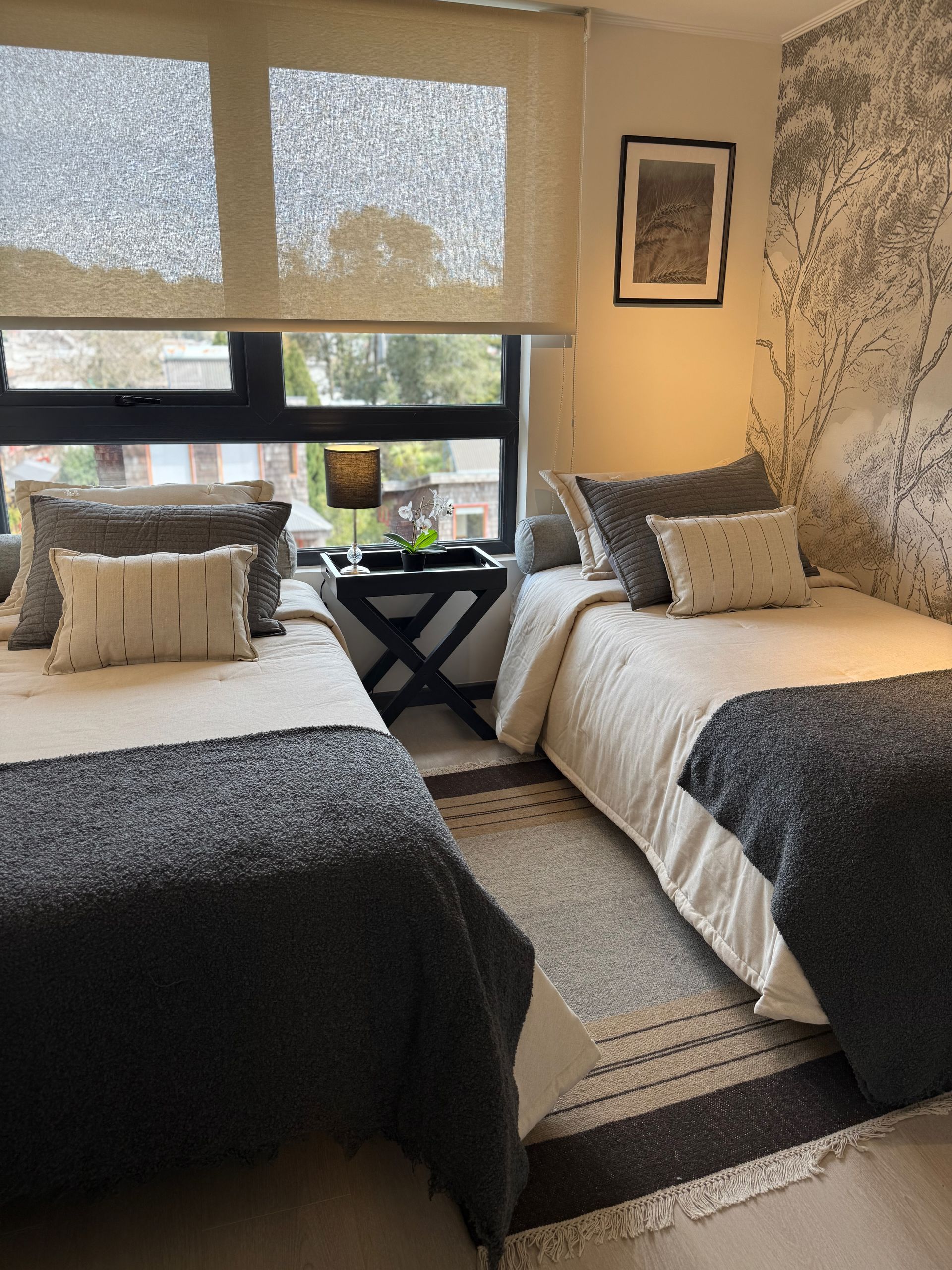 Dos camas individuales bien hechas en una acogedora habitación con ventana y decoración en tonos grises suaves.