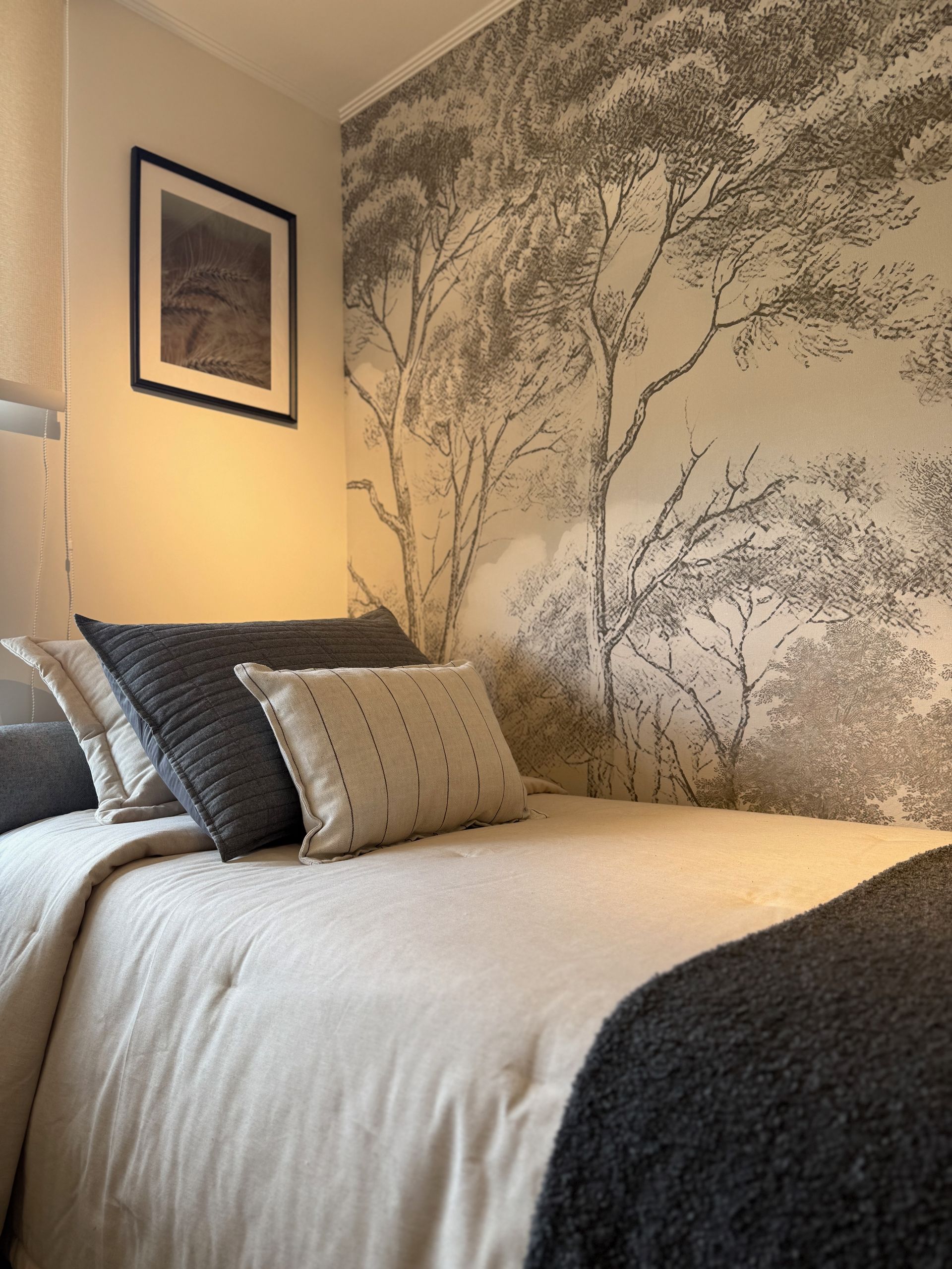 Habitación acogedora con una cama bien hecha, un mural botánico en la pared y una cálida iluminación con lámpara de noche.