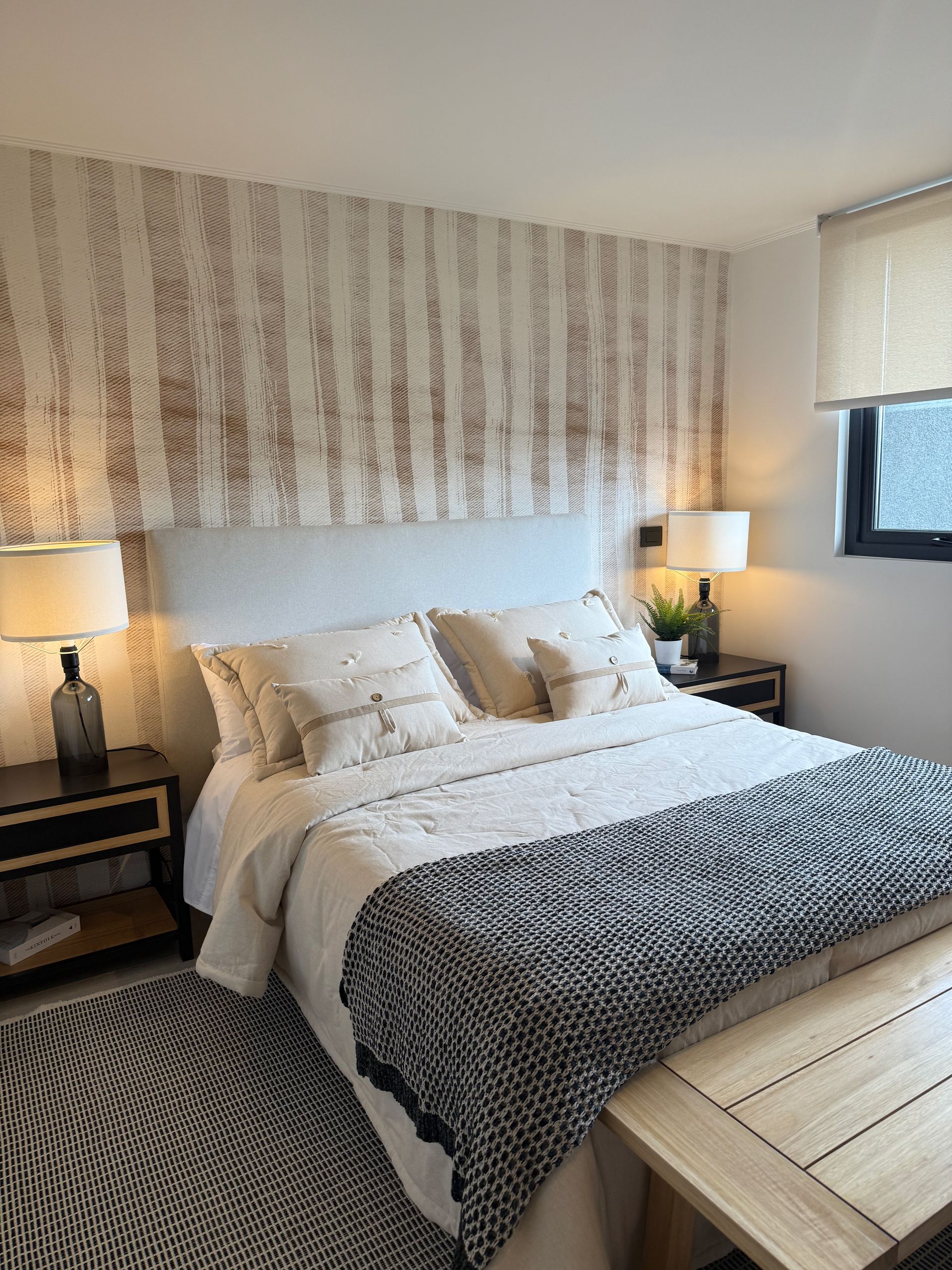 Habitación acogedora con una cama bien hecha, cabecero estampado, lámparas de noche y una ventana con persianas.