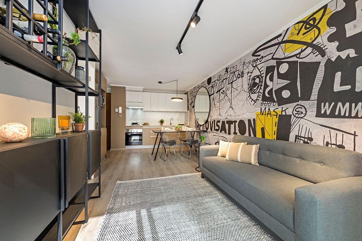 Sala de estar moderna con sofá gris, alfombra de cebra, mural en la pared y estanterías abiertas que dan al comedor.
