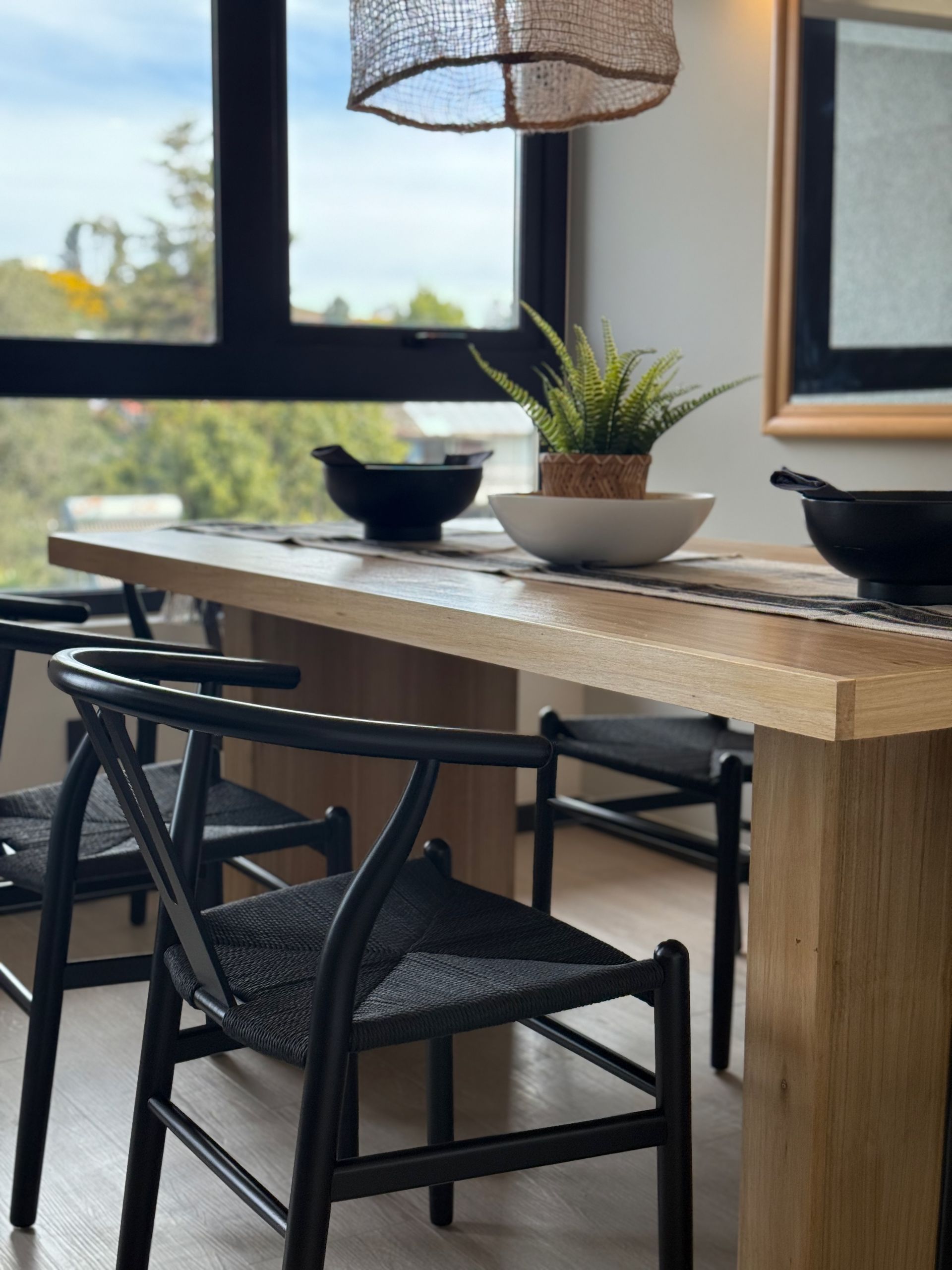 Sillas de comedor negras alrededor de una mesa rústica de madera junto a una ventana en una habitación luminosa.