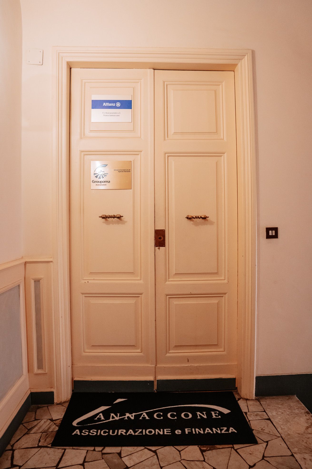Doppie porte color crema con insegne. Uno zerbino riporta la scritta 