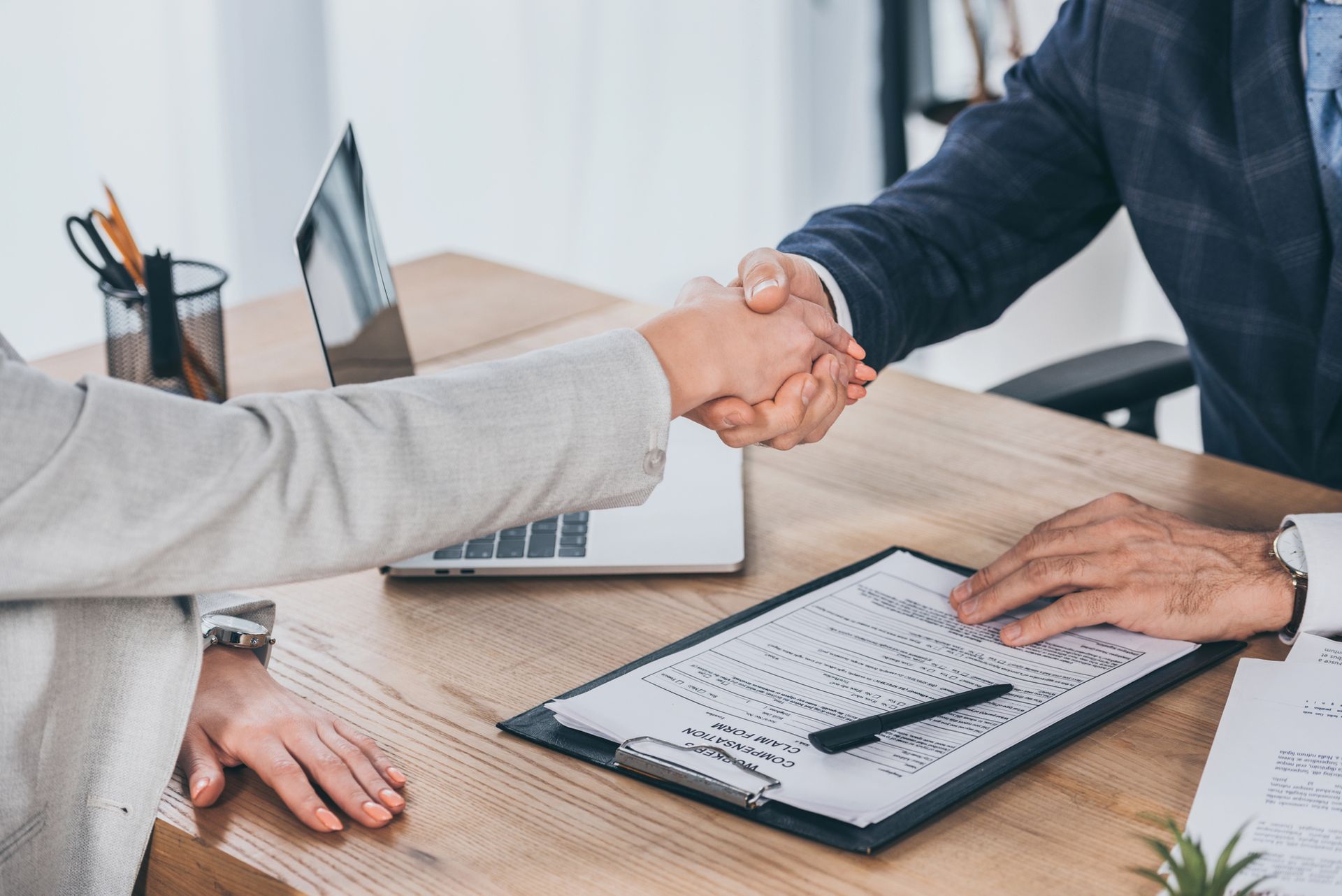 Due persone si stringono la mano per firmare un contratto su una scrivania, accanto a un computer portatile.