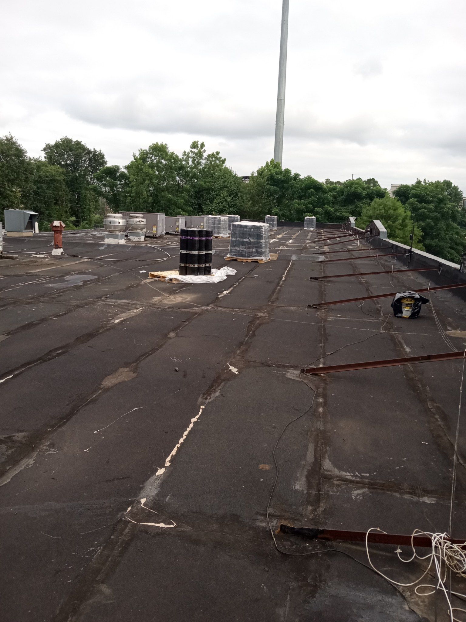 Flat rooftop with damaged black roofing, vents, and a cloudy sky in the background.