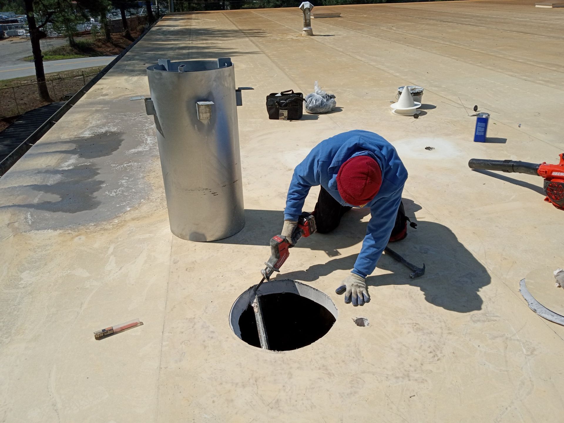 Worker kneeling beside a circular hole in a concrete pad, inspecting it with tools nearby.
