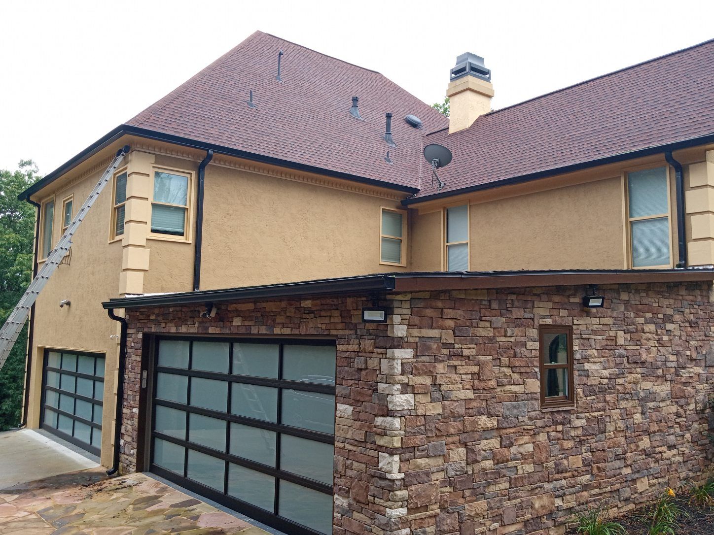 Large tan house with a red-tiled roof, stone garage, and frosted glass garage doors