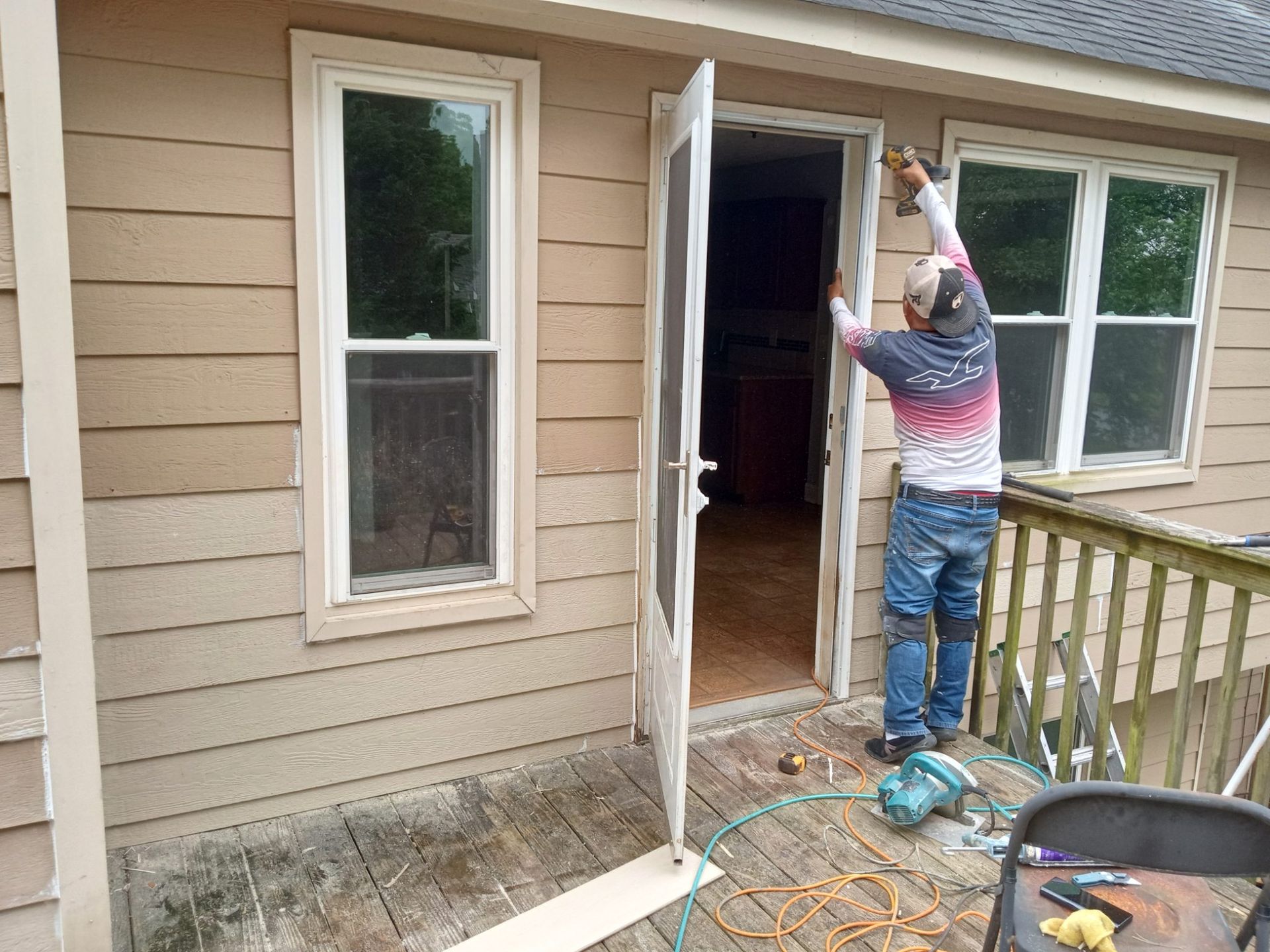 Person on porch painting a house exterior near an open door and window