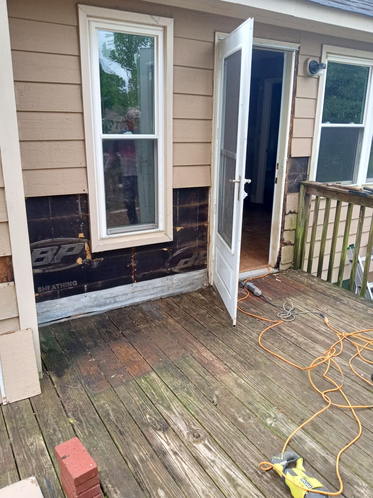 Back porch with open white door, weathered wood floor, and extension cord on the deck.