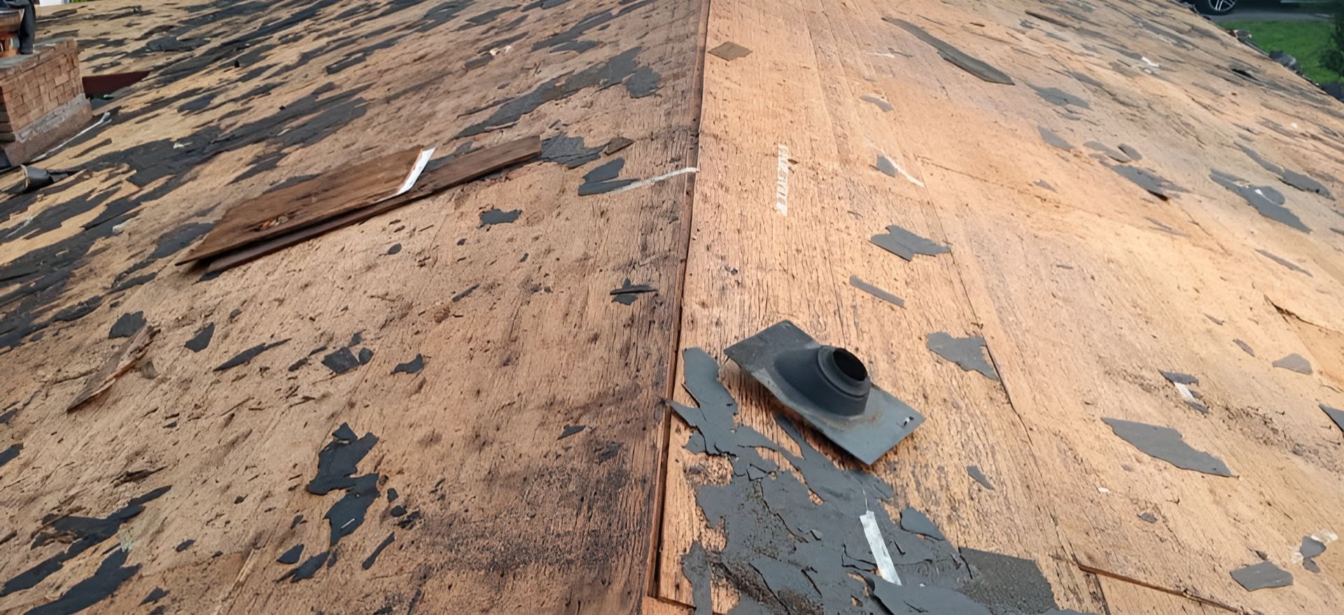 Close-up of a damaged brown rooftop with torn shingles and scattered debris.