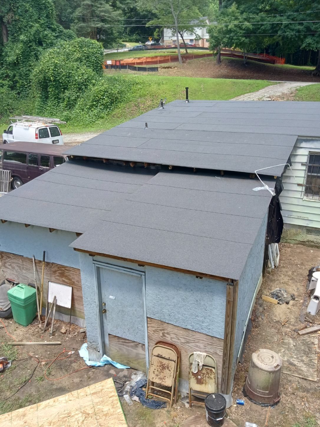Small gray shed with a black roof in a grassy rural area, seen from above, with a truck nearby