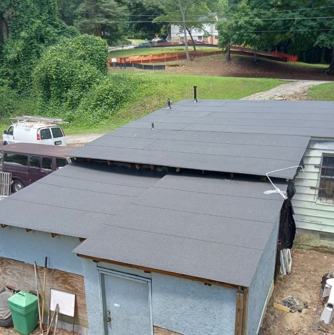 Gray roofed shed beside a gravel road, with a white truck and green trees in the background.