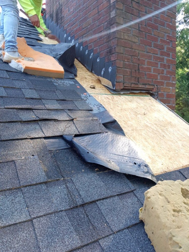 Roofing worker replacing damaged shingles on a house roof beside a brick chimney