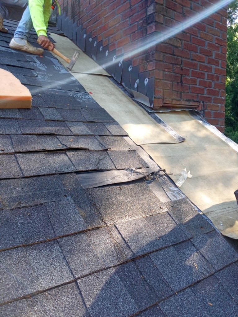 Worker spraying water on a shingled roof beside a brick chimney