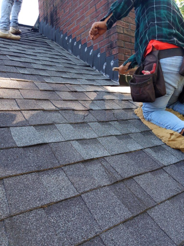 Roofers installing shingles on a sloped roof with a bucket and safety harnesses