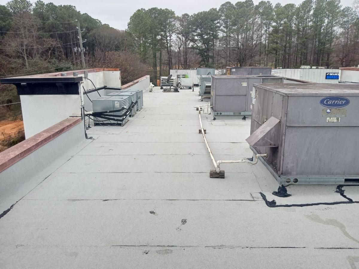 Rooftop with large HVAC units, vents, and pipes on a flat, gray roof surrounded by trees.