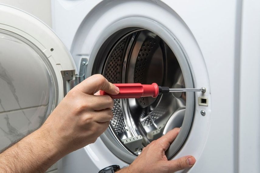 Person repairing a washing machine door with a screwdriver.