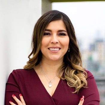 Una mujer con una camisa granate sonríe con los brazos cruzados.