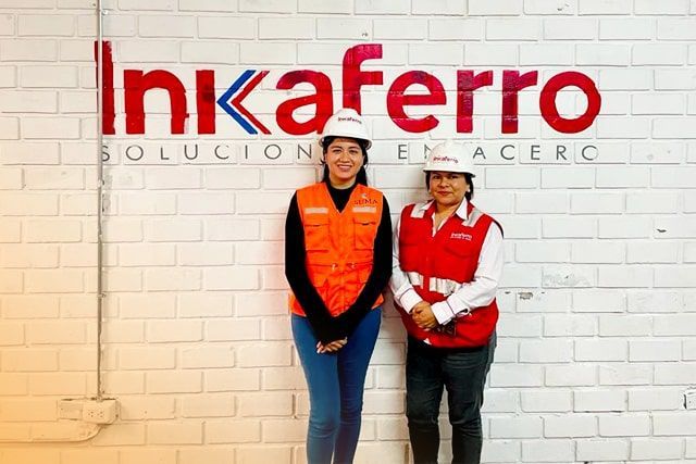 Dos mujeres paradas frente a una pared de ladrillos con Inkaferro escrito en ella