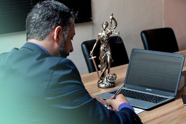 Un hombre está sentado en una mesa con una computadora portátil y una estatua de la justicia.