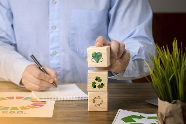 Un hombre está apilando bloques de madera con símbolos de reciclaje.