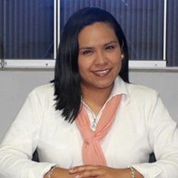 Una mujer vestida con una camisa blanca y un pañuelo rosa está sentada en un escritorio.