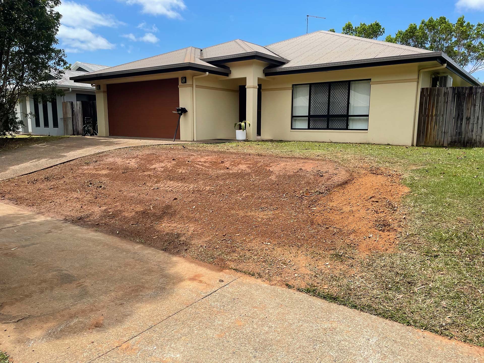 Single-story beige house with a brown garage door and a bare front yard, viewed from the driveway
