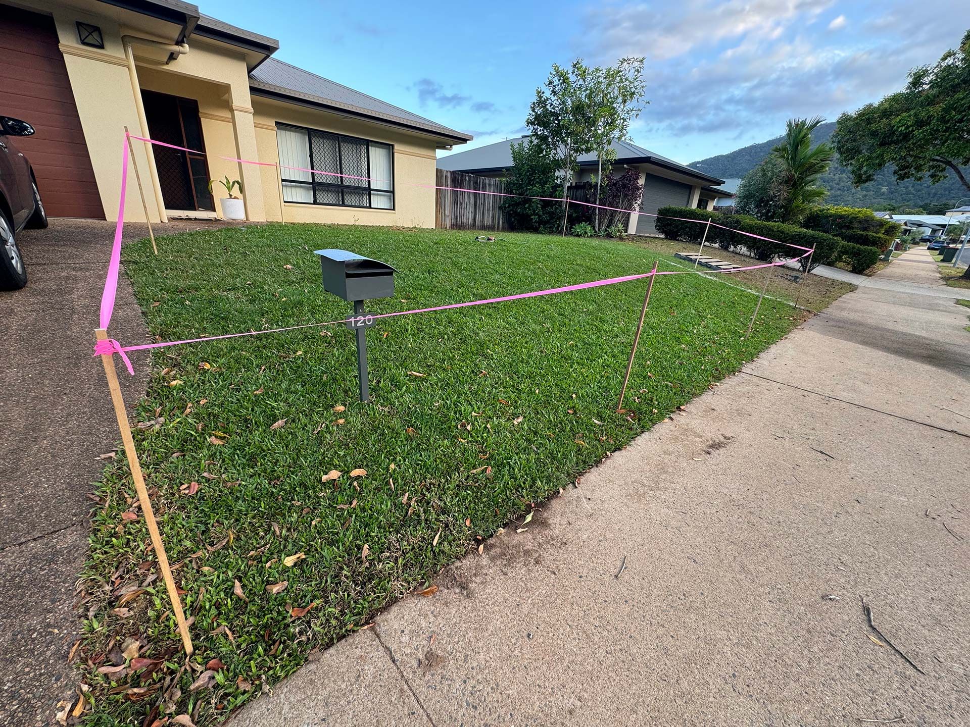 Front yard with a marked lawn area beside a house and sidewalk on a sunny day
