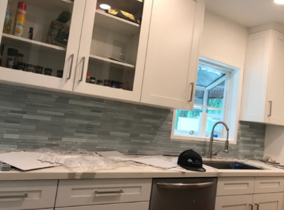 A kitchen with white cabinets , a sink , and a window.