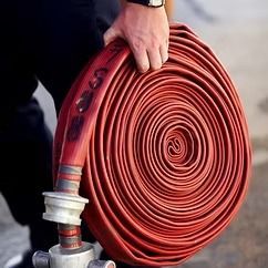 Coiled red fire hose held by a hand, with metal nozzle attached