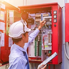 Technician inspecting an open red electrical control panel with tools in a factory setting