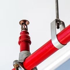 Red fire sprinkler pipe and sprinkler head mounted on a white ceiling