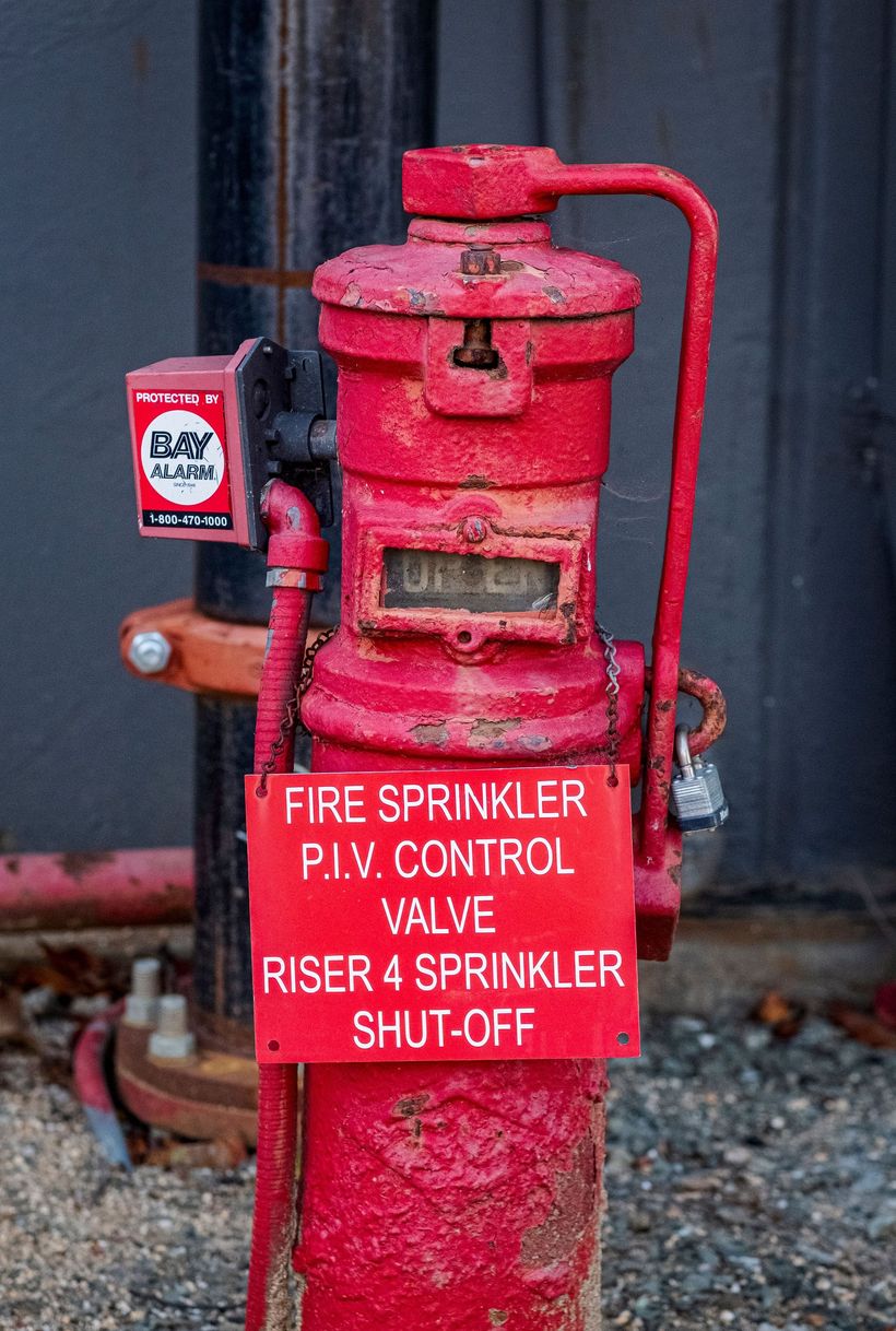 Red fire sprinkler valve riser with white warning sign in an industrial setting