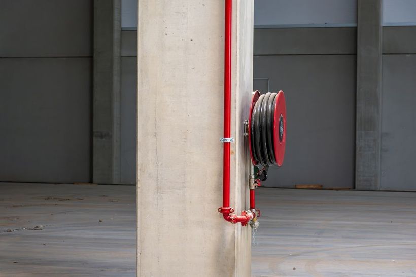 Red fire hose reel mounted on a concrete pillar in an indoor garage-like space