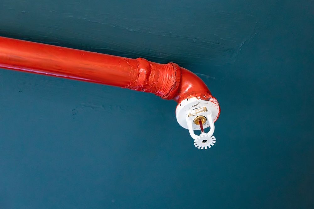 Red fire sprinkler pipe with a white sprinkler head against a blue ceiling