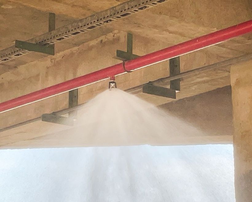 Red pipe sprinkler spraying water in an indoor industrial ceiling area