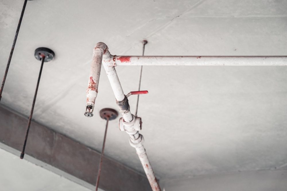 Ceiling pipe with red valve and exposed plumbing in a concrete parking garage