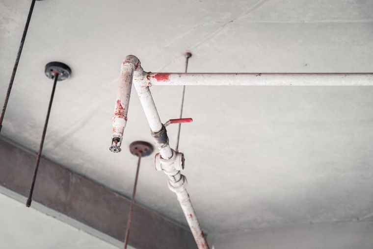 Ceiling pipe with red valve and exposed plumbing in a concrete parking garage