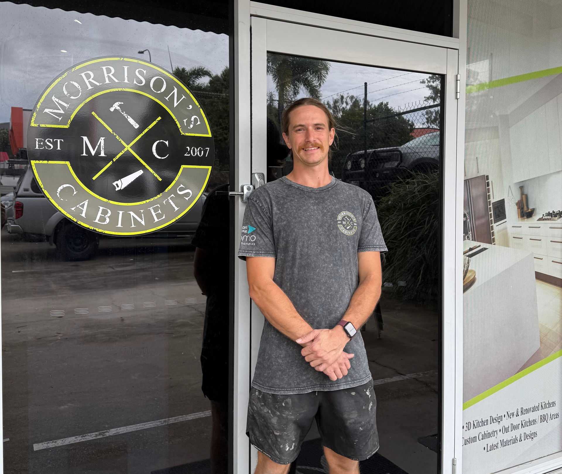 Man standing outside Morrison’s Cabinets storefront, wearing a gray T-shirt and black shorts.