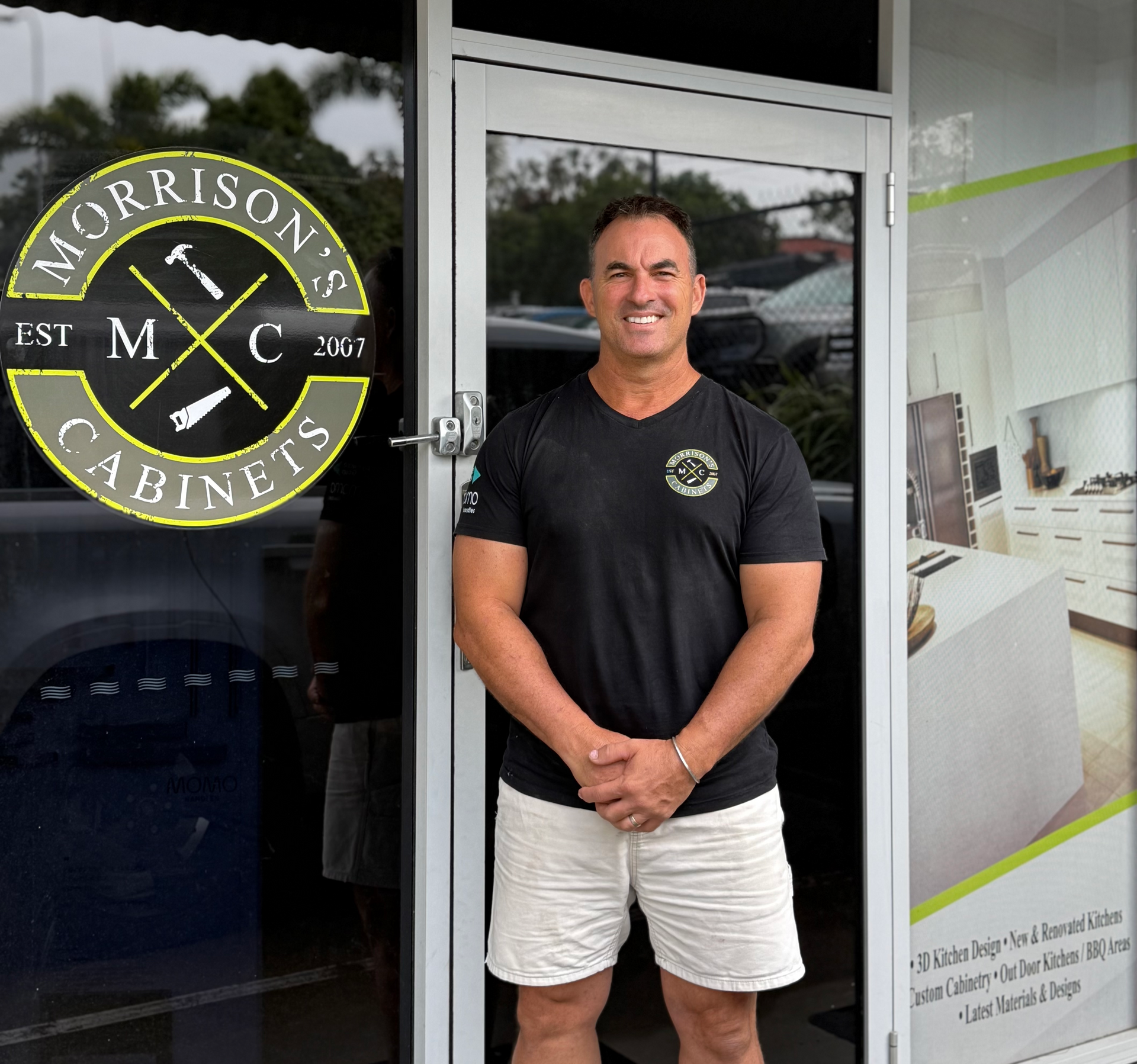 Man standing at the entrance of Morrison Cabinets, wearing a black shirt and white shorts.